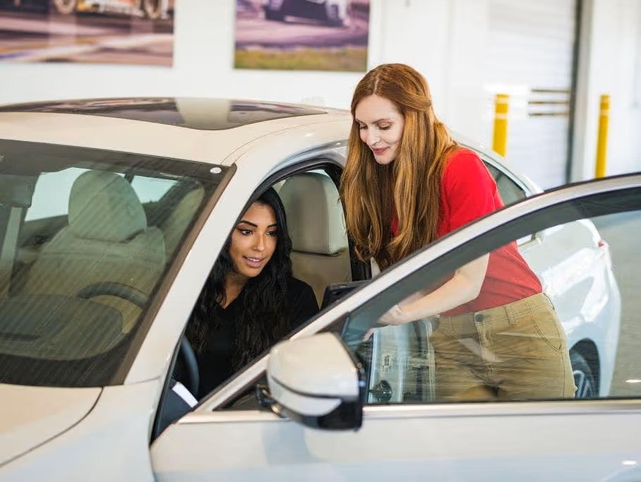 Two people standing next to an open car door inside the showroom