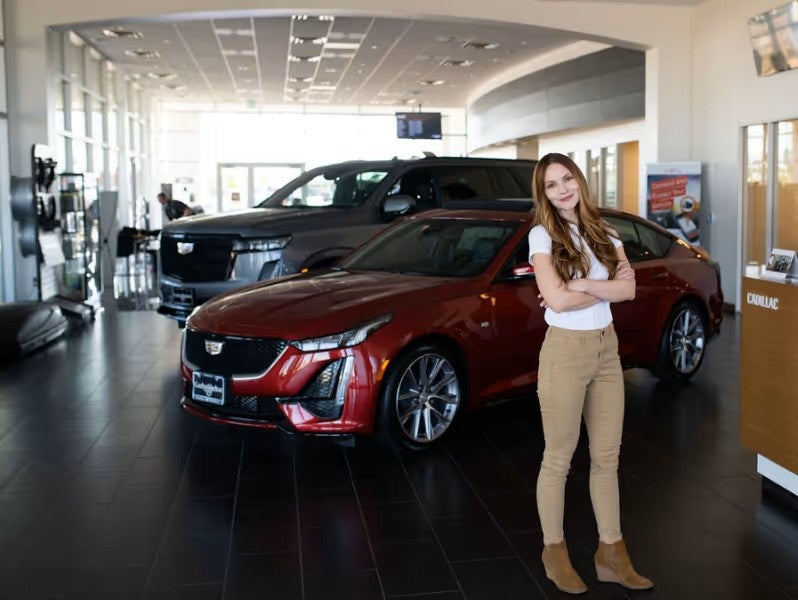 A person standing indoors in front of a shiny red car displayed in the showroom