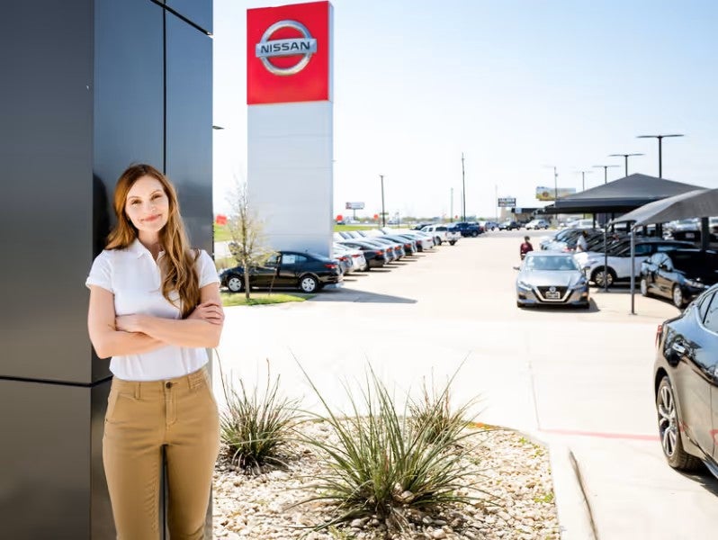 A person standing outdoors in front of a tall red-and-white Nissan sign