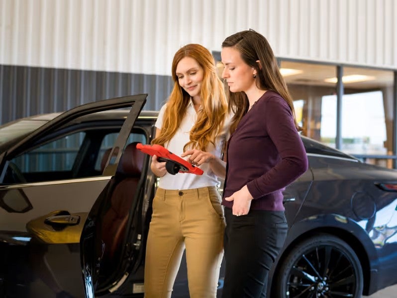Two people standing next to an open car door inside the dealership